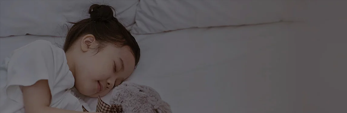 어린아이가 침대에서 곰 인형을 안고 잠들어 있는 모습입니다.
